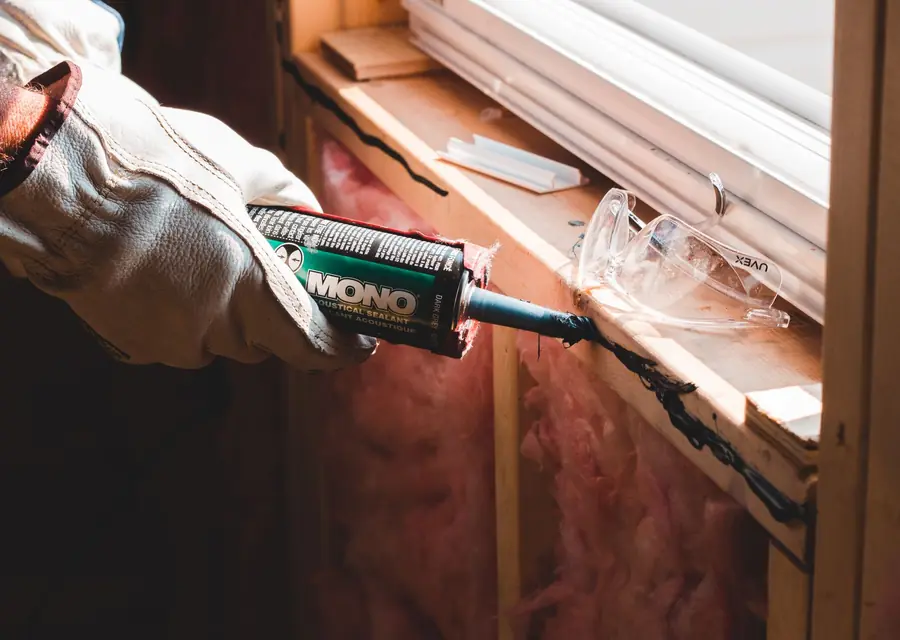 Gloved hand sealing a gap around a window frame with a caulk gun to keep rats out